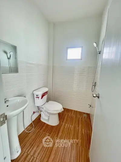 Modern bathroom with white tiles and wooden flooring, featuring a shower and toilet.