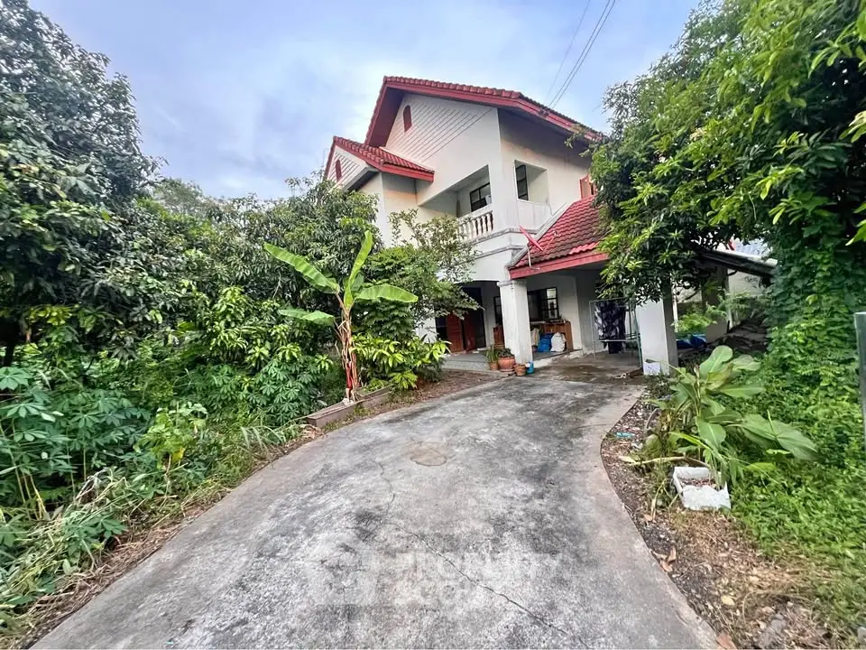 Charming two-story house with red roof surrounded by lush greenery and spacious driveway.