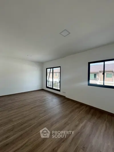 Spacious empty room with wooden flooring and large windows offering natural light.