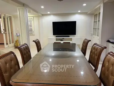 Elegant dining room with glass-top table and leather chairs, featuring a large wall-mounted TV.