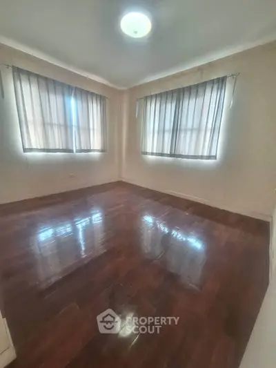 Spacious empty room with polished wooden floors and large windows, perfect for customization.