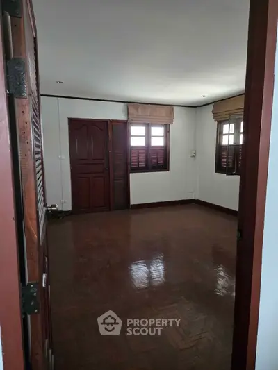 Spacious empty room with wooden flooring and large windows, perfect for customization.
