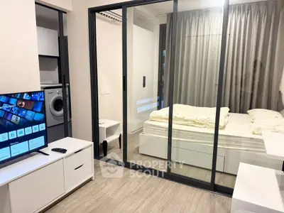 Modern studio apartment with glass partition, featuring a cozy bedroom and in-unit washing machine.