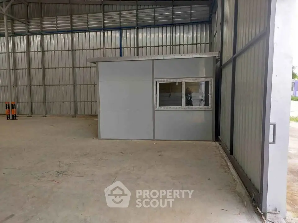 Spacious industrial warehouse interior with small office cabin and high ceilings.