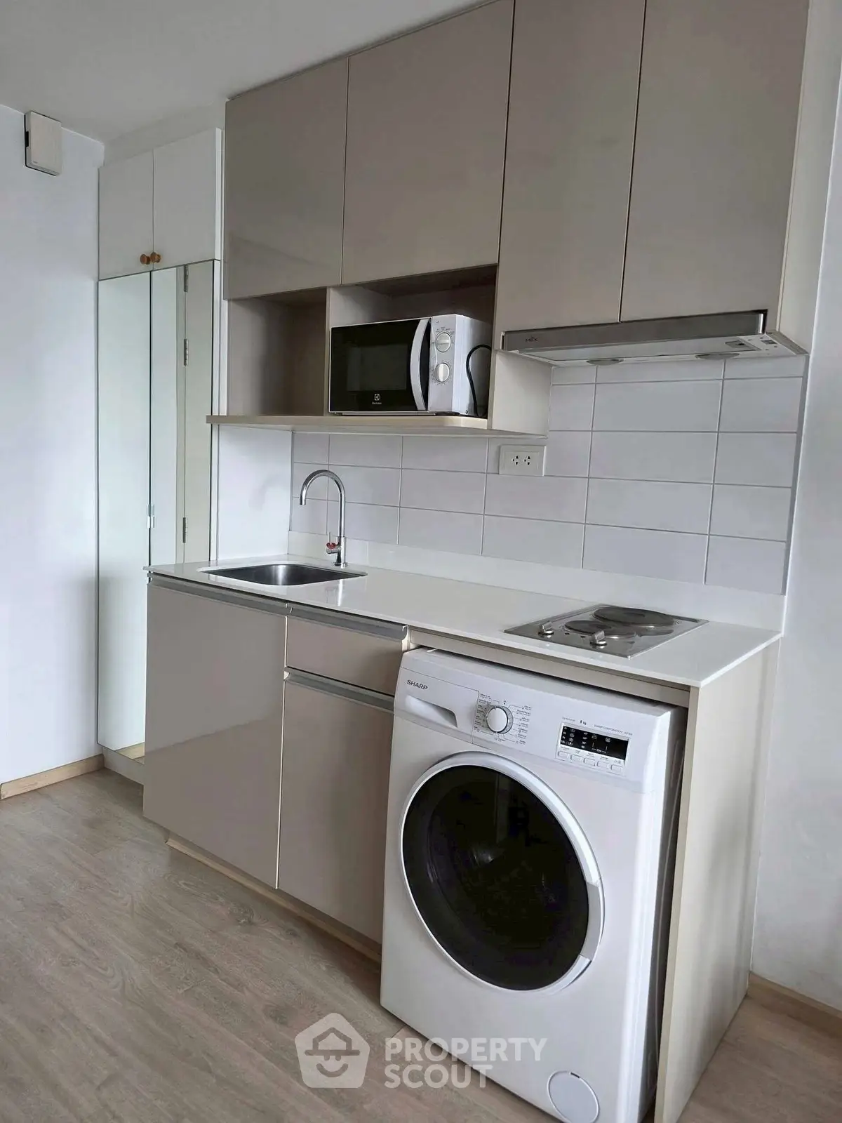 Modern compact kitchen with washing machine and microwave in sleek apartment.