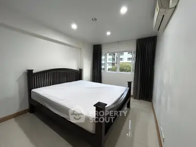 Spacious bedroom with large window and modern furnishings in a well-lit apartment.