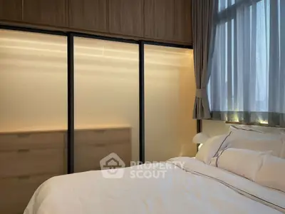 Elegant bedroom with soft lighting and large window, featuring modern built-in wardrobes and cozy bedding.