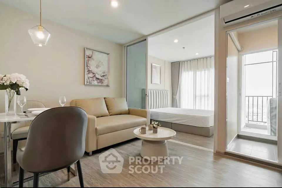 Modern open-plan living room with cozy seating and elegant decor, leading to a bright bedroom with balcony view.