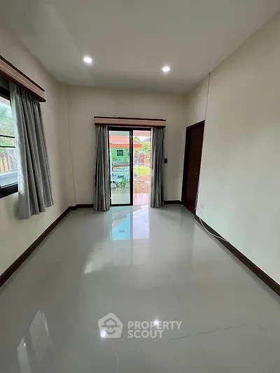 Spacious empty room with glossy tiled floor and sliding glass doors leading to a garden view.