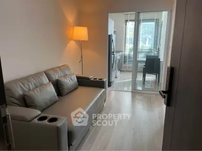 Modern living room with sleek sofa and view into a bright kitchen area.