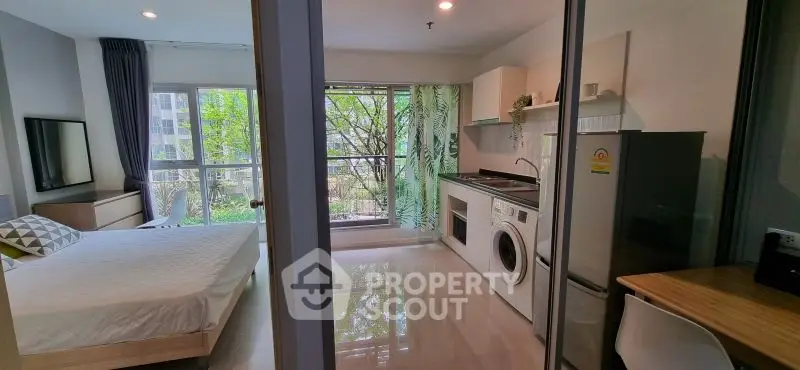 Modern studio apartment with open layout, featuring a cozy bedroom and fully equipped kitchen with lush green views.