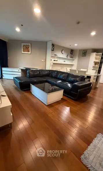 Spacious living room with elegant wooden flooring and modern black leather sofa.
