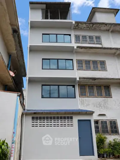 Modern multi-story building exterior with sleek windows and a blue door, showcasing urban architecture.
