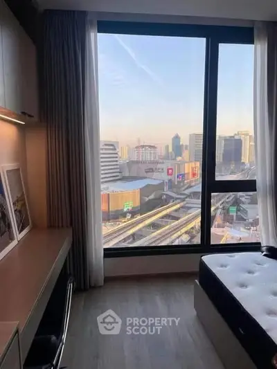 Modern bedroom with city view, featuring large window and sleek furnishings.