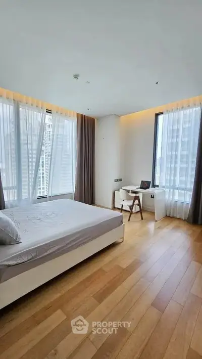 Spacious bedroom with large windows and wooden flooring in modern apartment