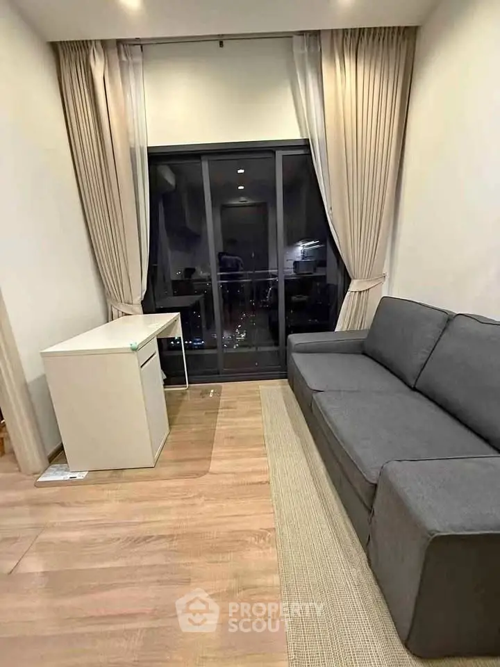Modern living room with sleek gray sofa and large window offering city view.