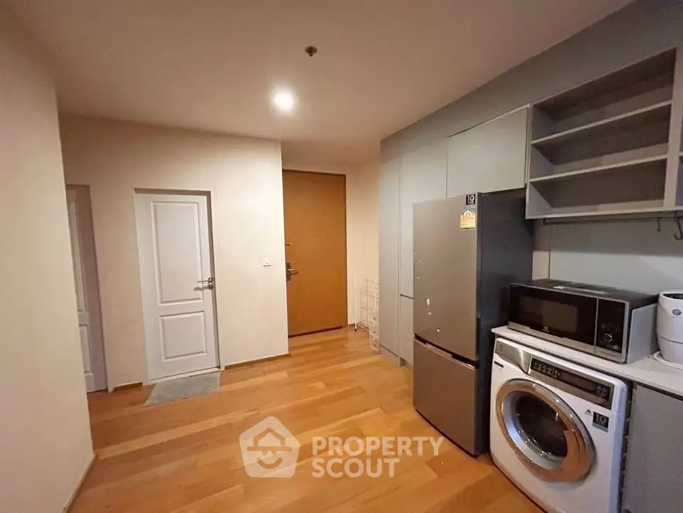 Modern kitchen with washing machine and microwave, featuring sleek cabinetry and wooden flooring.