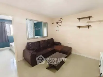 Modern living room with brown leather sofa and glass coffee table, adjacent to a bedroom.