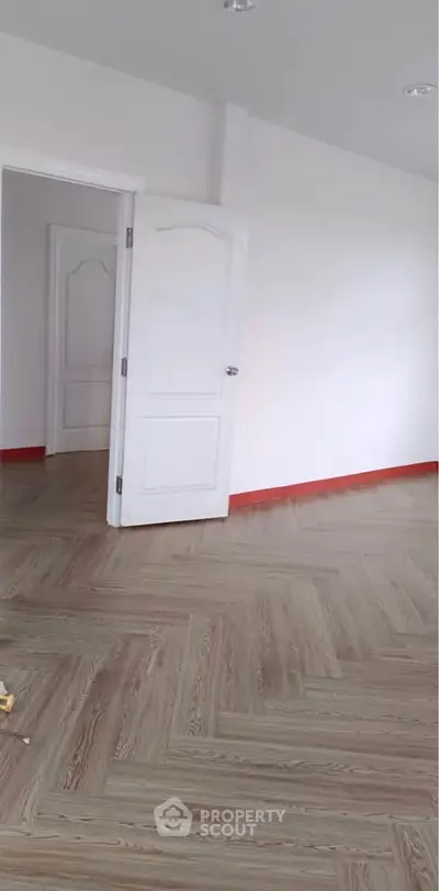 Spacious empty room with elegant wooden flooring and white walls.