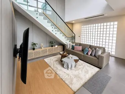 Modern living room with stylish decor and open staircase, featuring a cozy seating area and elegant design.