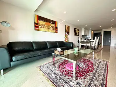 Spacious modern living room with elegant decor and dining area, featuring a luxurious black leather sofa and stylish artwork.