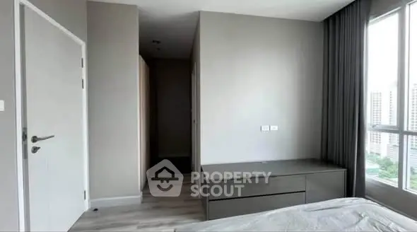 Modern bedroom with sleek furniture and large window offering city views.