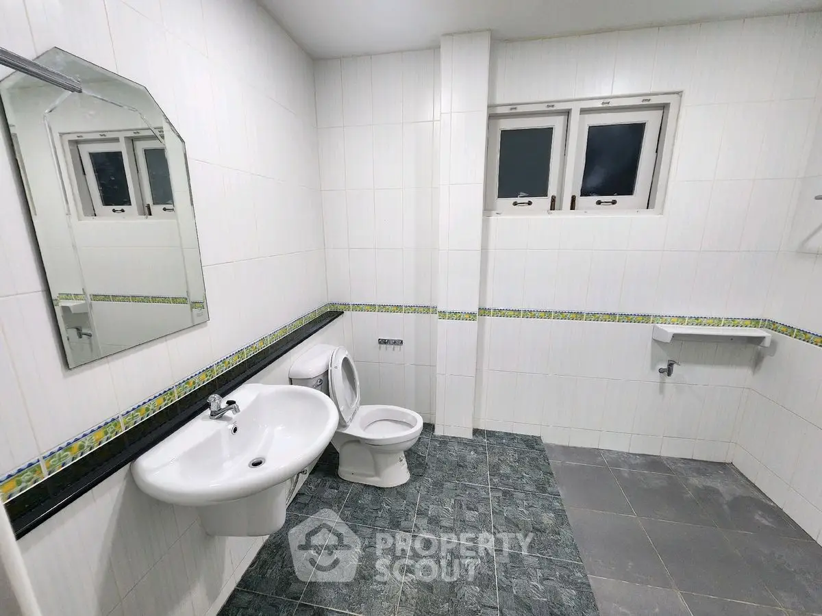 Spacious bathroom with modern fixtures and tiled walls, featuring a large mirror and window for natural light.