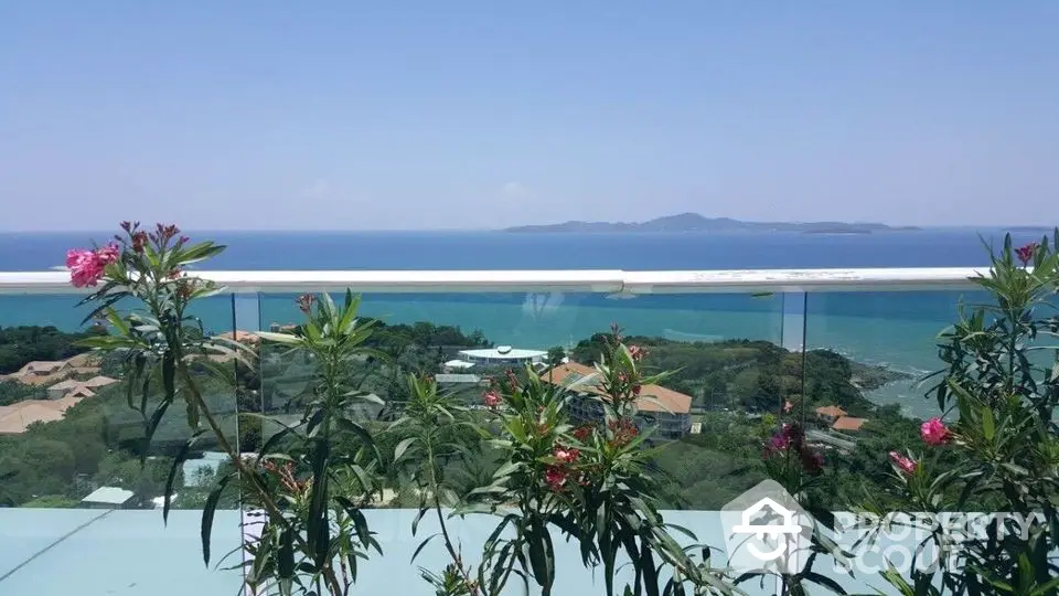 Stunning ocean view from a modern balcony with glass railing and lush greenery.