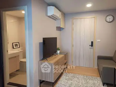 Modern living room with TV, air conditioning, and bathroom access in cozy apartment.