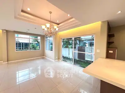Spacious living room with elegant chandelier and garden view through large windows.