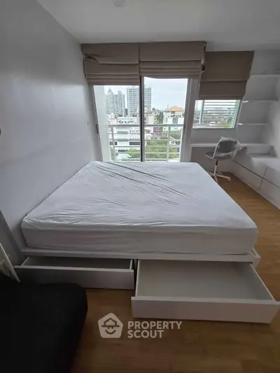 Modern bedroom with city view, featuring a sleek bed with storage drawers and a stylish chair by the window.
