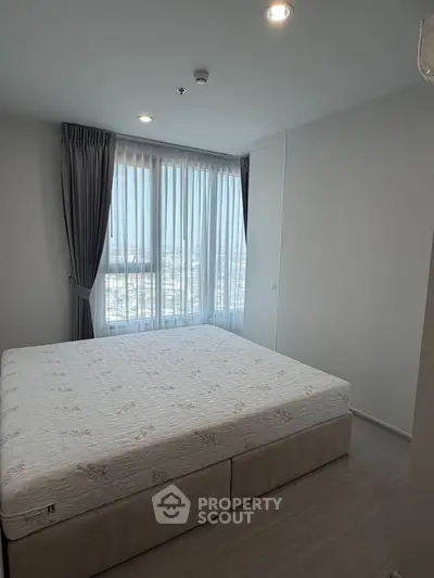 Spacious bedroom with large window and modern decor in high-rise apartment.