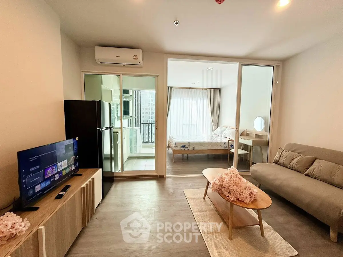 Modern living room with open layout to bedroom and kitchen, featuring stylish furniture and natural light.