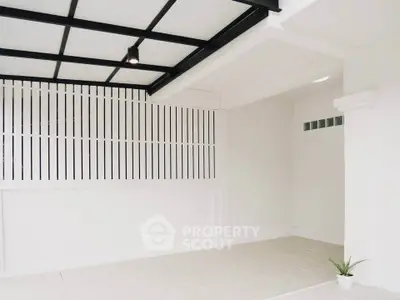 Modern minimalist interior with white walls and black ceiling beams, featuring a small potted plant.