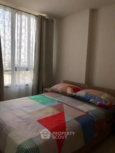 Cozy bedroom with colorful bedding and natural light from large window.