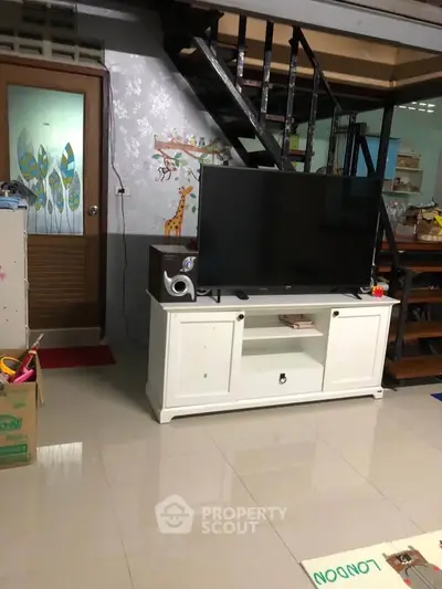 Charming living room with modern TV setup and stylish staircase, perfect for cozy family gatherings.