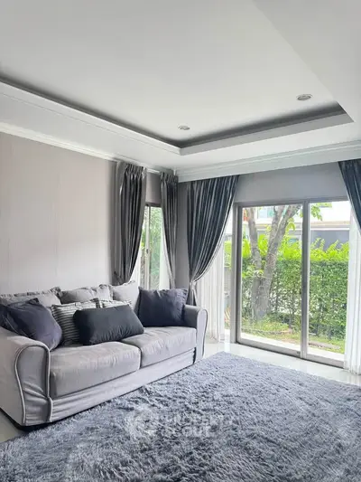 Elegant living room with plush sofa and large windows overlooking lush greenery.