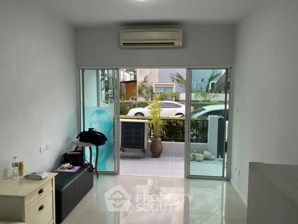 Modern living room with large glass doors opening to a small patio, featuring sleek air conditioning unit.