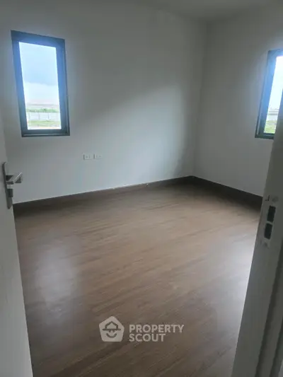 Spacious empty room with wooden flooring and two windows offering natural light.