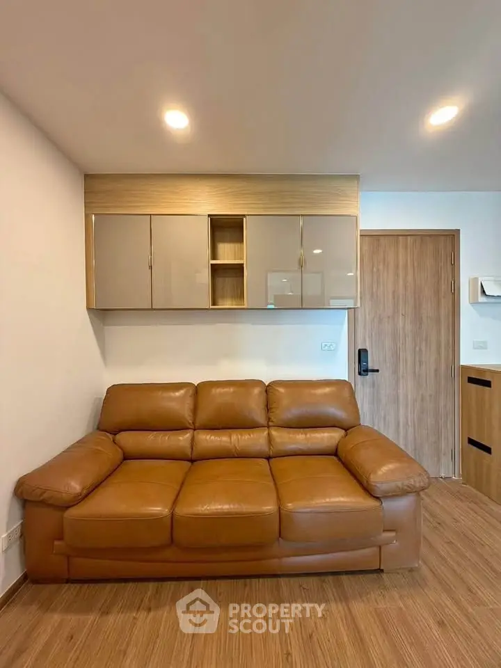 Modern living room with brown leather sofa and wooden flooring, featuring sleek wall cabinets.