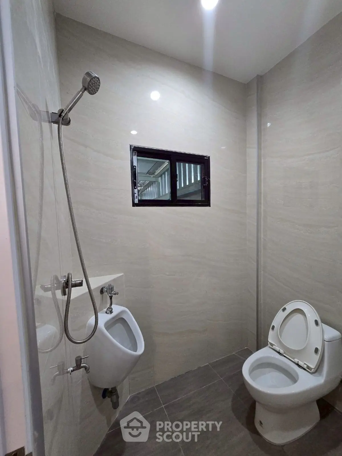 Modern bathroom with sleek fixtures and neutral tiles, featuring a toilet and urinal.