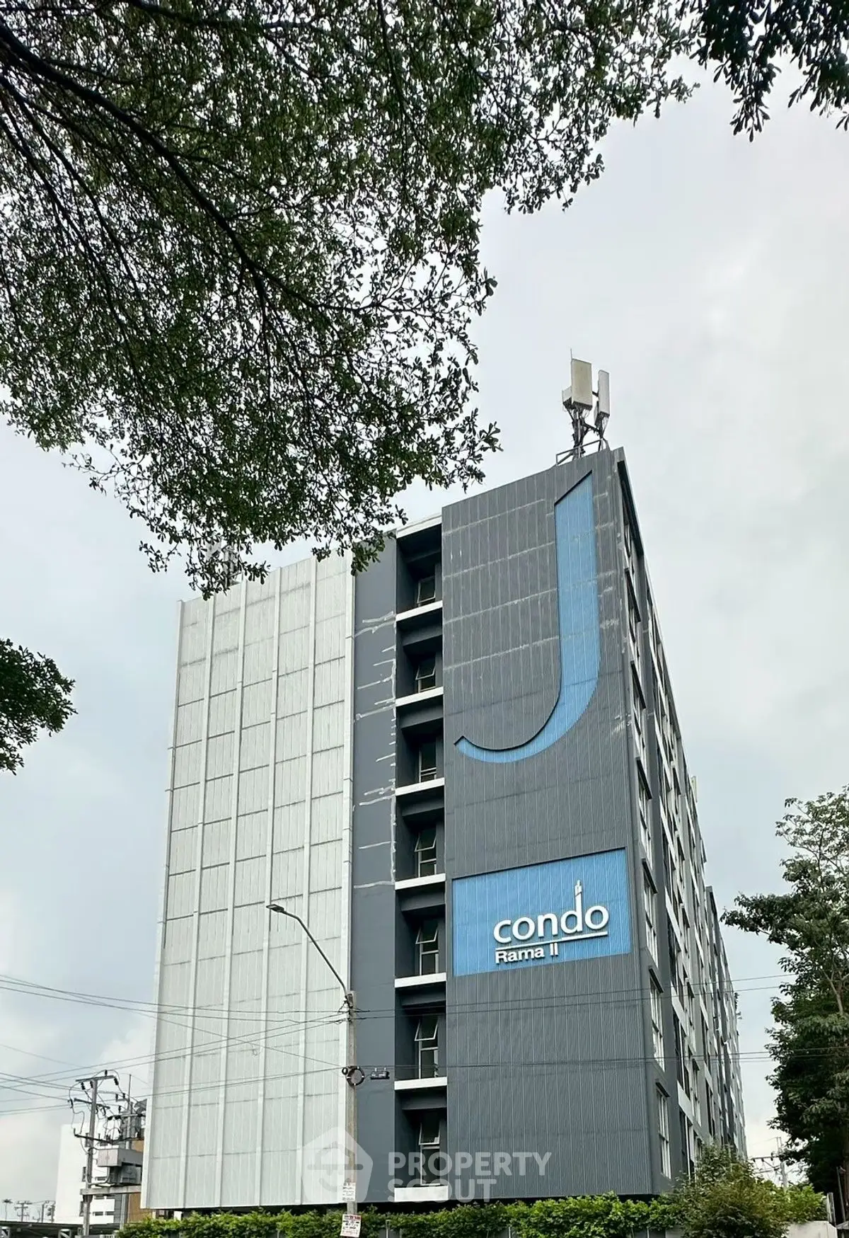 Modern condo building with sleek design and prominent logo, surrounded by lush greenery.