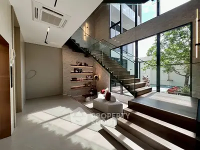 Luxurious modern living room with elegant staircase and large windows offering abundant natural light.