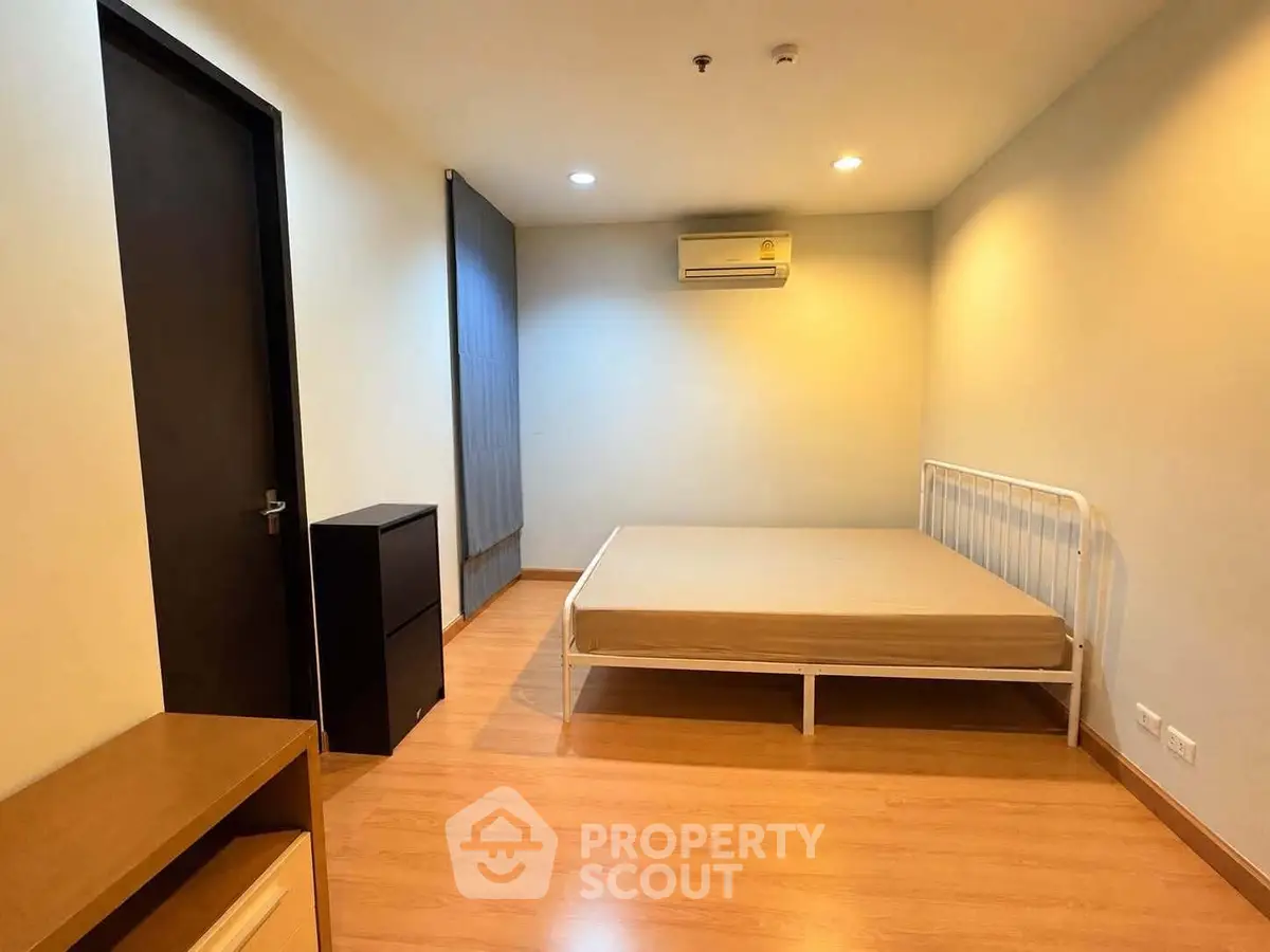Spacious bedroom with minimalist design and wooden flooring, featuring a bed and air conditioning.
