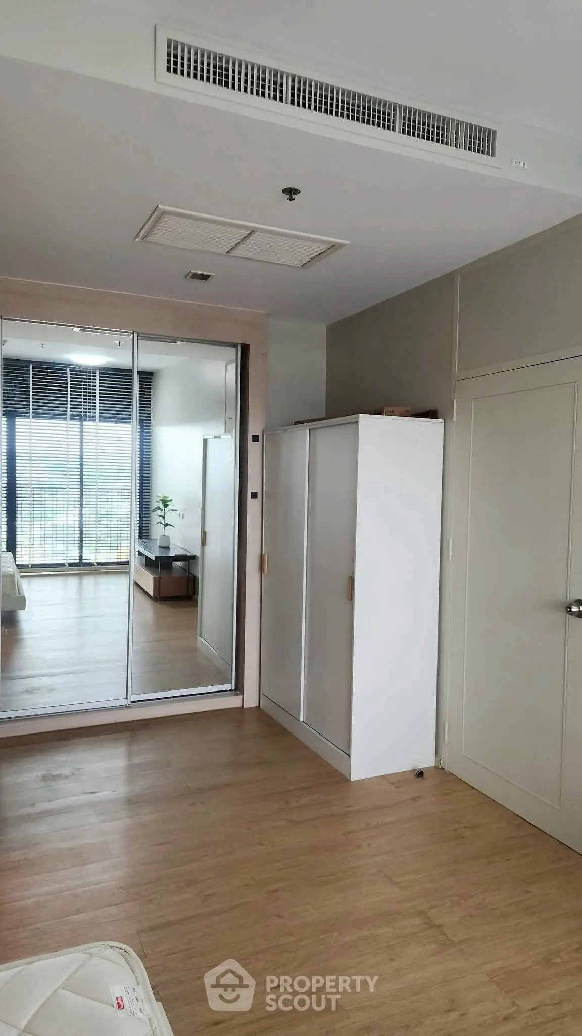 Modern bedroom with mirrored wardrobe and wooden flooring, offering a sleek and spacious design.