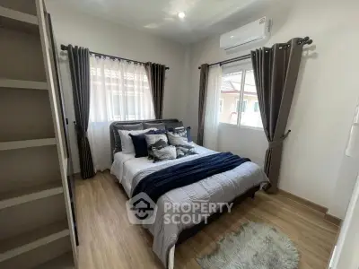 Cozy bedroom with stylish decor and natural light, featuring wooden flooring and modern air conditioning.