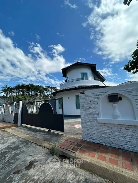 Charming white house with unique architecture and spacious driveway under a vibrant blue sky.