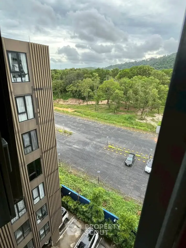 Scenic view from high-rise building overlooking lush greenery and parking area.
