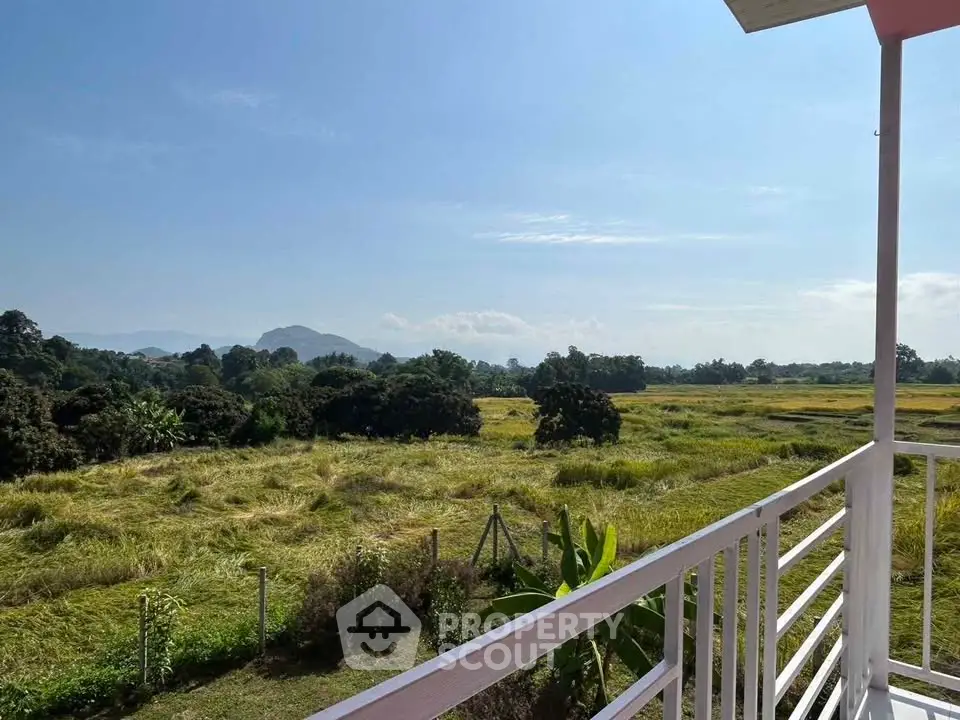 Scenic balcony view overlooking lush green fields and distant mountains, perfect for nature lovers.