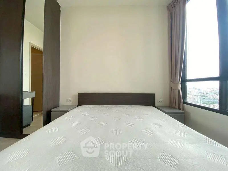 Spacious bedroom with large window offering city view, modern furniture, and natural light.